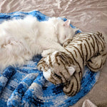 White cat laying on a blanket and cuddling with a Snuggle Kitty anxiety relief pet toy