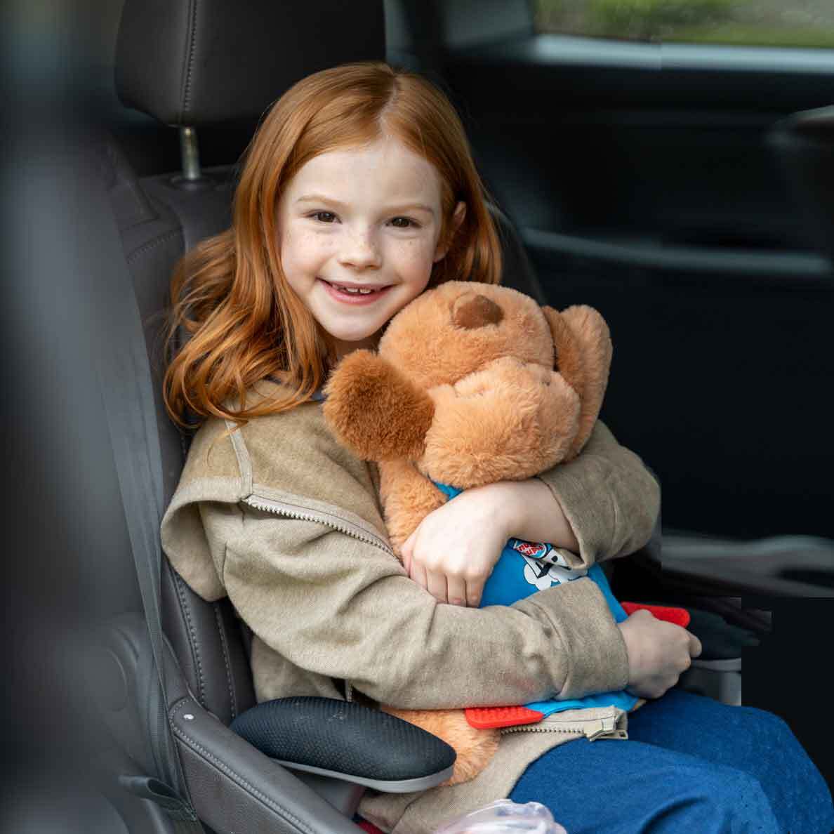 Young girl sitting in car hugging her Snuggle Puppy Hero