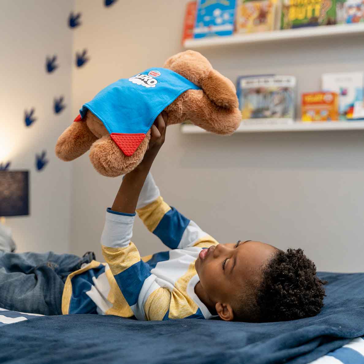 Young boy laying on his bed holding up a Snuggle Puppy Hero in the air
