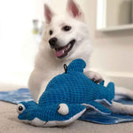 White dog laying down and playing with blue hammerhead shark plush dog toy
